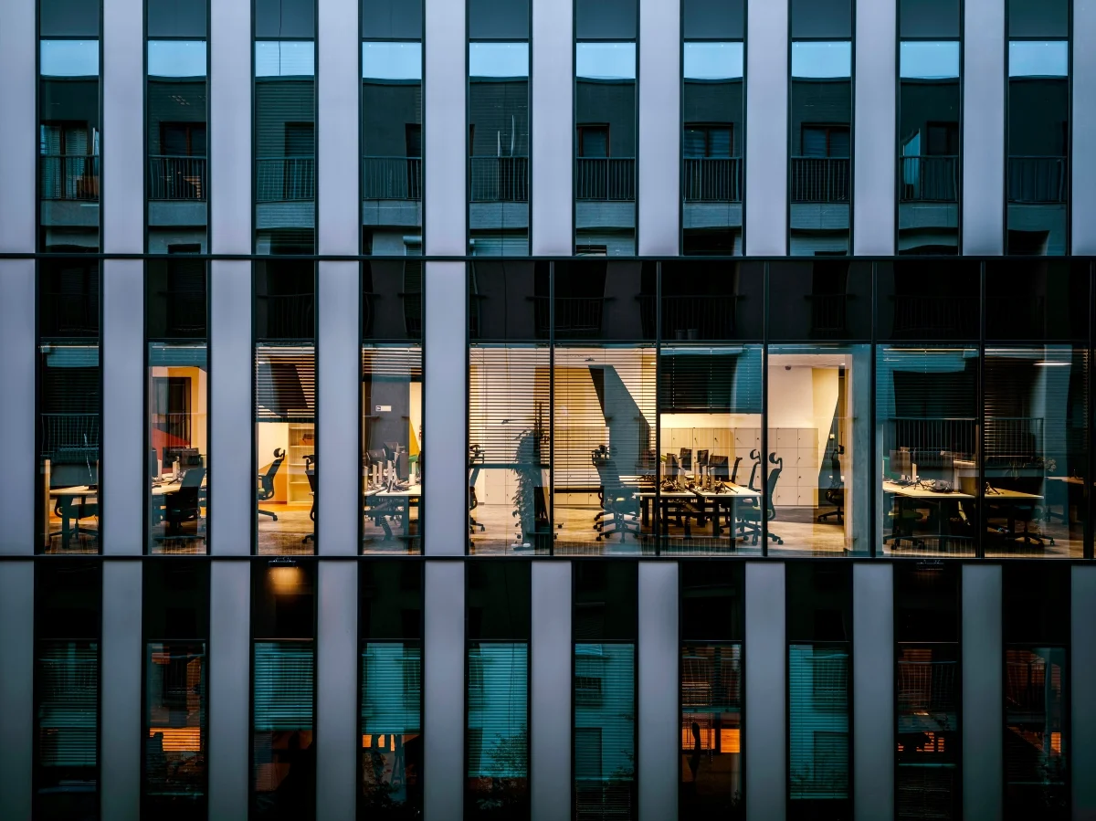 An office building at dusk with lit floors behind a glass facade